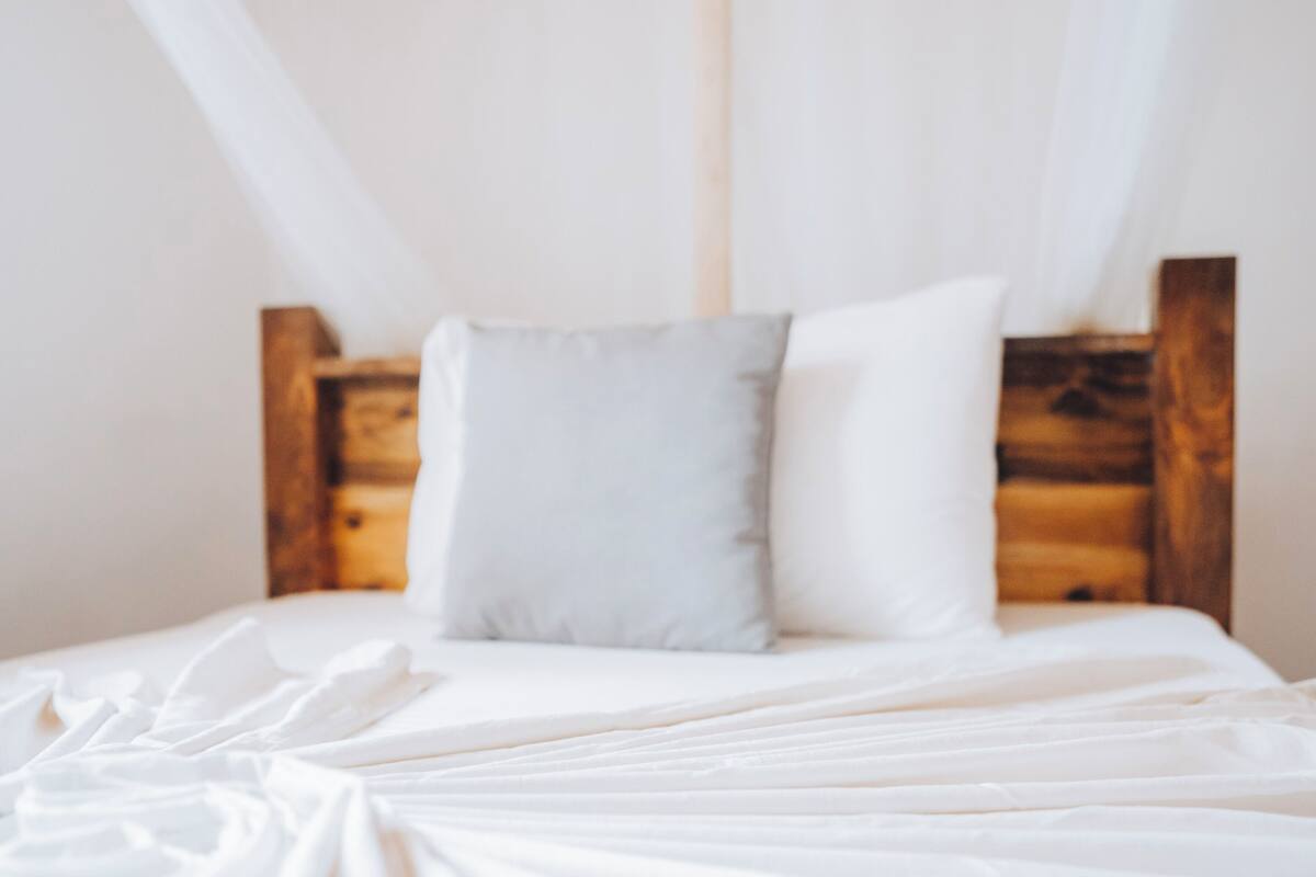 A bed with white bedding and wooden headboard, a grey pillow, and a white pillow.