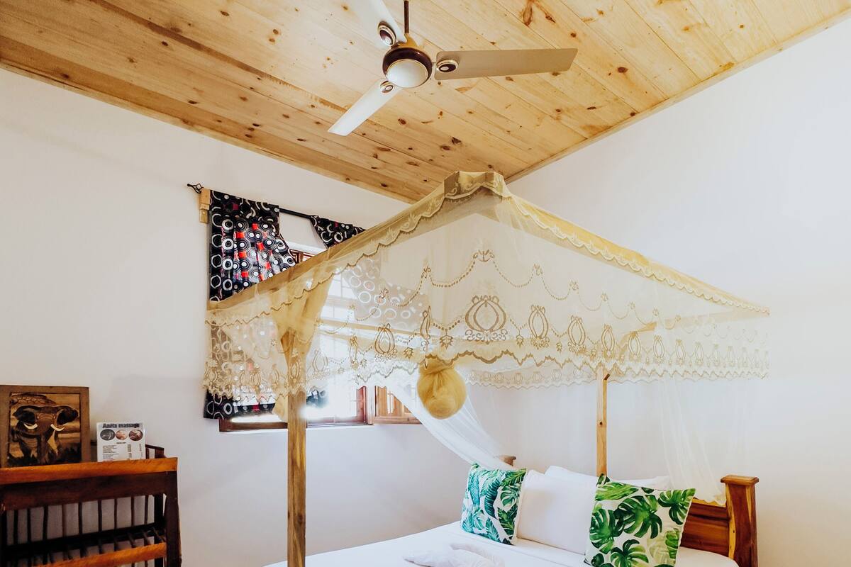 A wooden ceiling with a ceiling fan, a bed with a canopy, and a wooden nightstand with a basket.