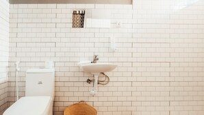 Une salle de bain avec des murs recouverts de carreaux blancs, des toilettes blanches, un lavabo blanc et un plancher en bois.