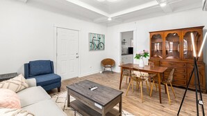 Un salon comprenant un canapé, une table basse, une table à manger avec des chaises, un meuble et un tableau accroché au mur.