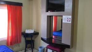 Una habitación de hotel con cama, escritorio, silla, televisor y espejo.
