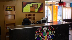 Una recepción con una decoración colorida de 'Dia de Muertos', un estante de madera con figuritas y un cuadro abstracto grande en la pared.