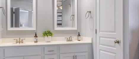 A bathroom with two sinks, a mirror, a potted plant, and a door.