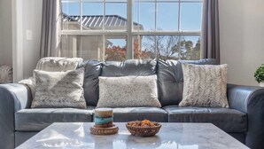 Ein modernes Wohnzimmer mit einem grauen Ledersofa, gemusterten Kissen und einem Marmortisch.