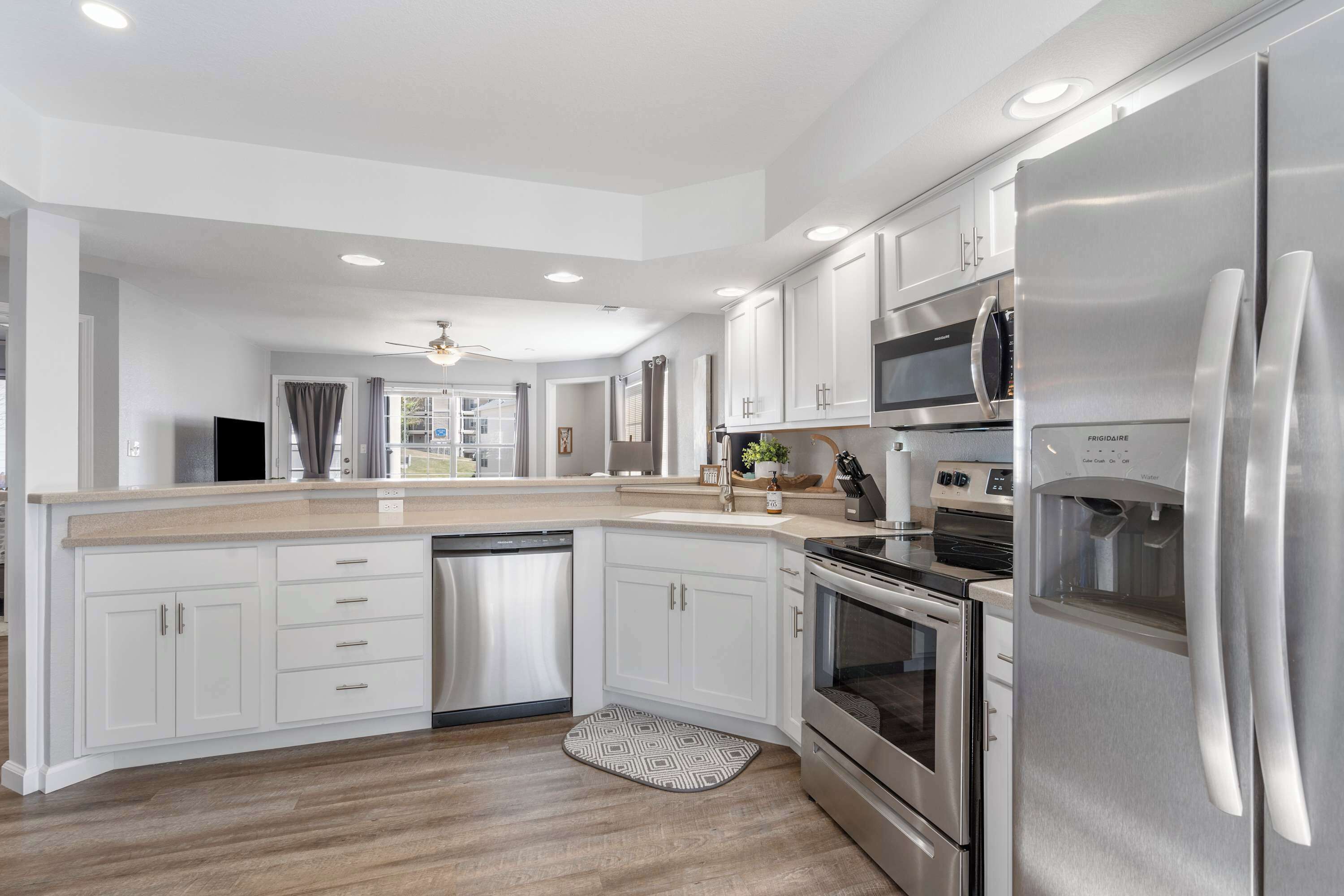 A modern kitchen with white cabinets, stainless steel appliances, and a wooden floor.