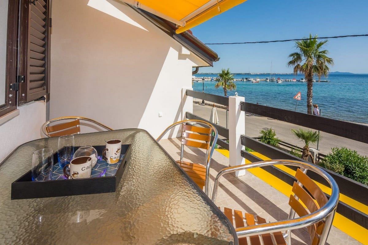 A balcony with a table, chairs, and a view of the sea.