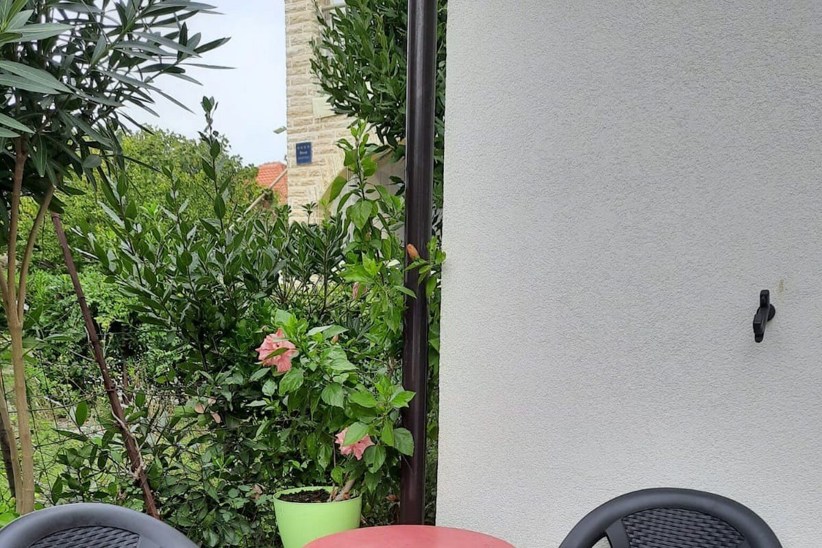 A small outdoor patio with two black plastic chairs and a round table with a red tablecloth.