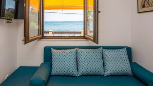 Un sofá azul verdoso con cojines estampados, una ventana con persiana amarilla y un cuadro en la pared.