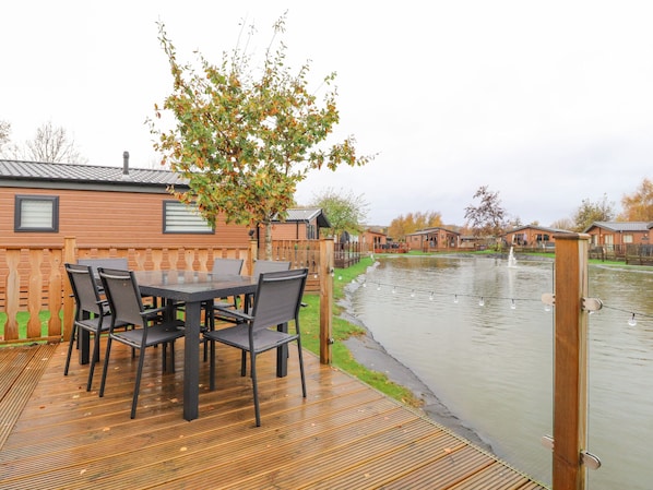 A wooden deck with a table and chairs, a wooden fence, and a canal with houses in the background.
