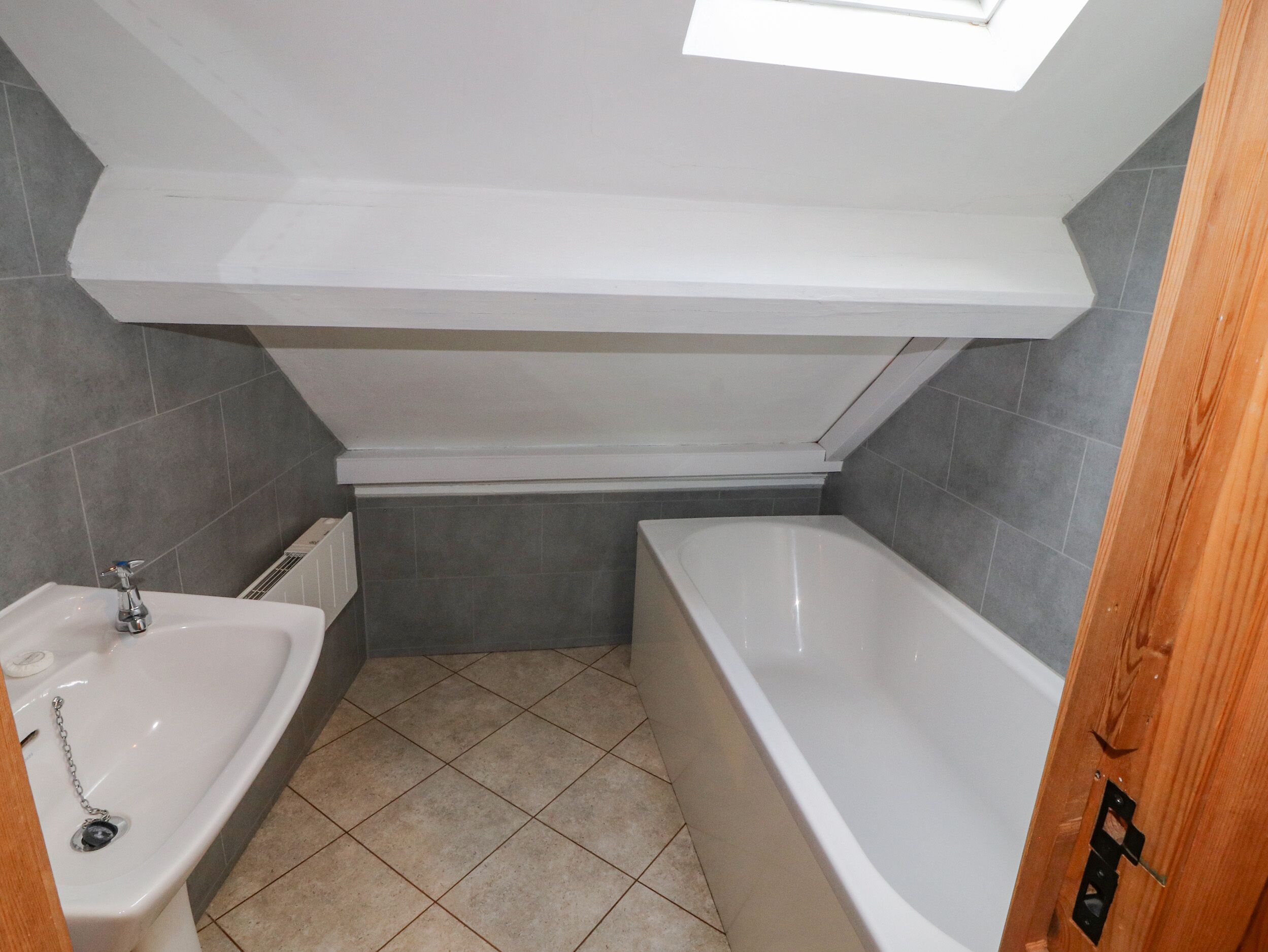 A bathroom with a bathtub, a sink, and a skylight.