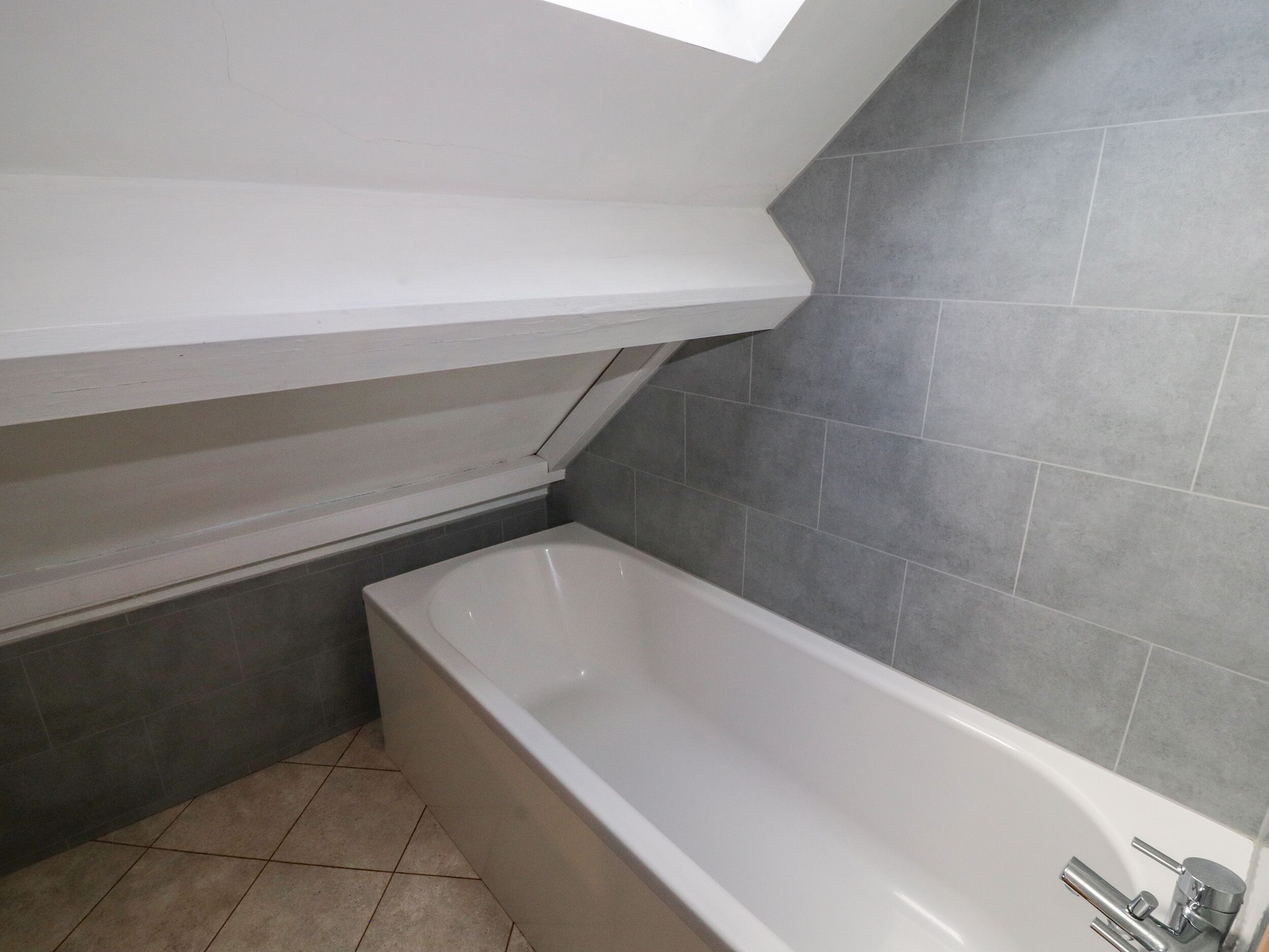 Un baño moderno con una bañera independiente, paredes de azulejos grises y un tragaluz sobre la zona de la ducha.