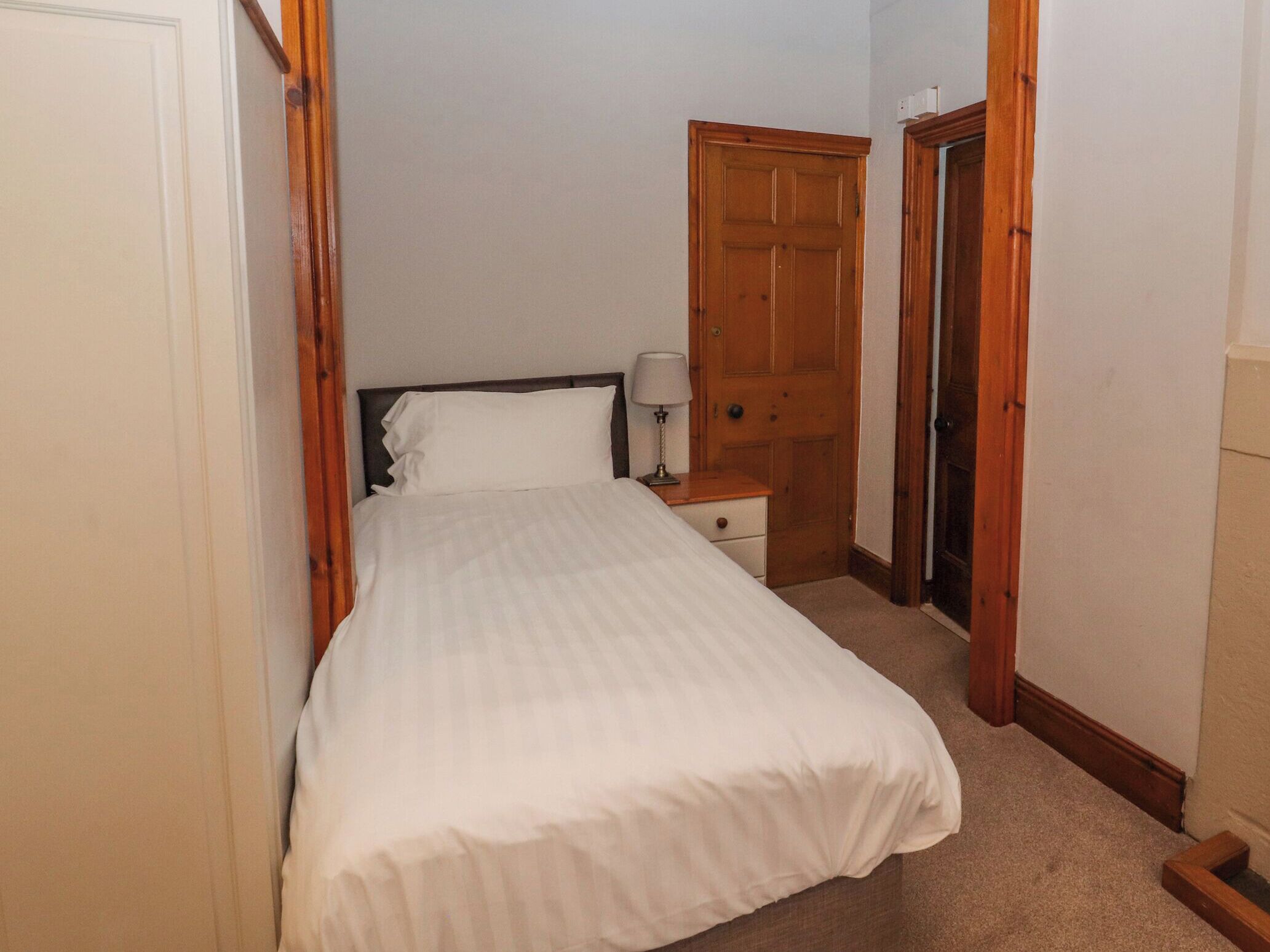 A bedroom with a bed, a nightstand, a lamp, and a wooden door.