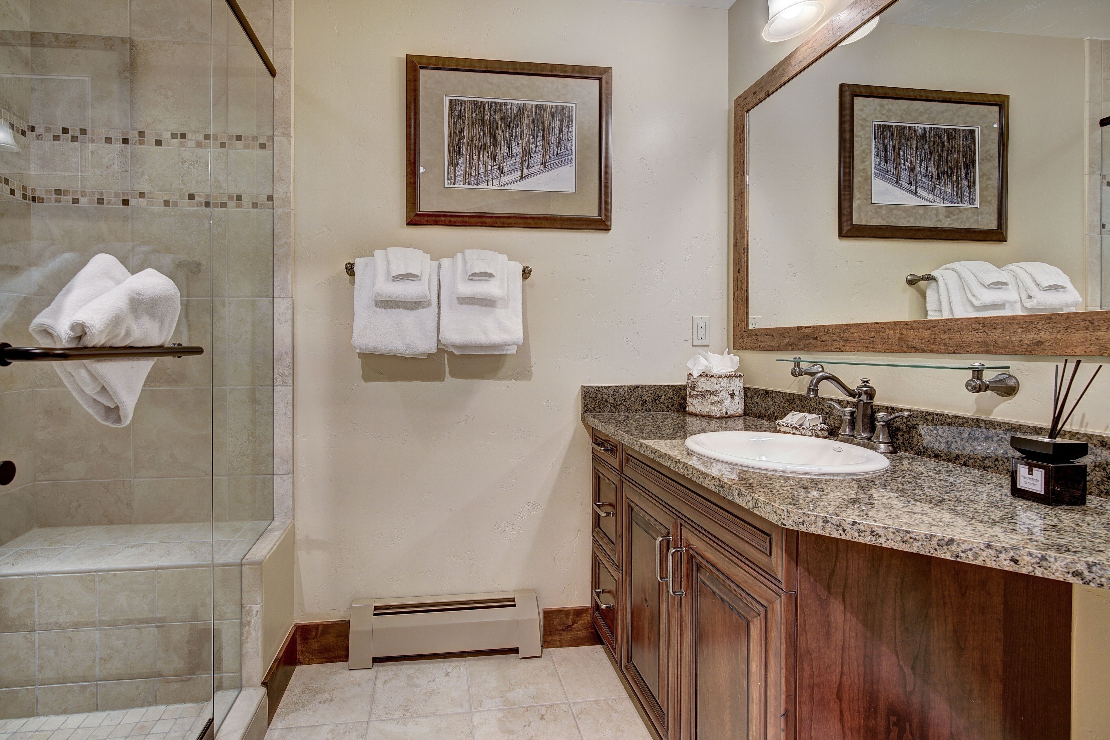 A bathroom with a glass shower enclosure, a sink with a vanity, and two framed pictures on the wall.