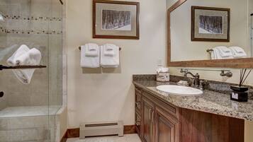 A bathroom with a glass shower enclosure, a sink with a vanity, and two framed pictures on the wall.