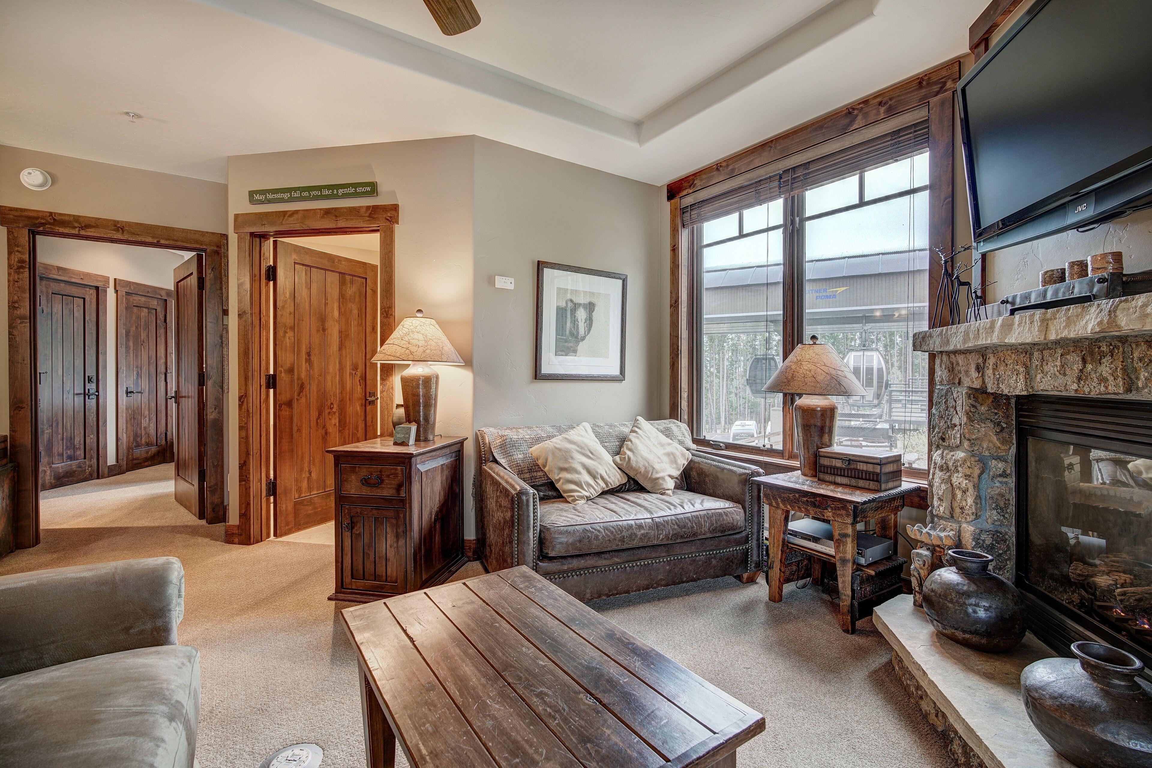 A cozy living room with a fireplace, wooden furniture, and a large window.
