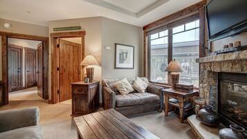 A cozy living room with a fireplace, wooden furniture, and a large window.
