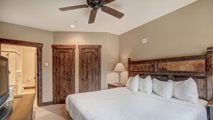 A bedroom with a large bed, wooden wardrobe, a ceiling fan, a bedside lamp, and a TV on a wooden stand. - True Ski-in/ski-out Luxury Condo On Peak 7 1 Bedroom Condo by RedAwning (Breckenridge)