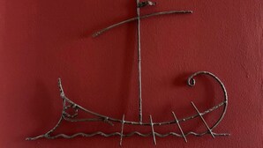 Una escultura de metal que representa un barco sobre un muro rojo.