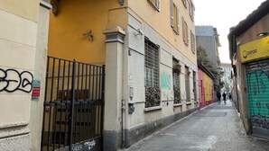 Un estrecho callejón flanqueado por edificios, destacando una construcción amarilla con ventanas protegidas por rejas y un portón cerrado.