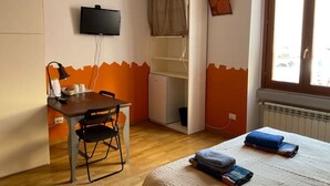 Una habitación con cama, escritorio con silla, televisión, armario y ventana con cortinas.