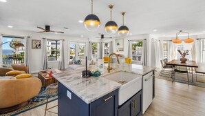 A modern kitchen with a central island, pendant lights, and a view to the outside.
