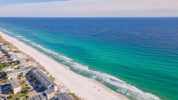 A coastal residential area with houses along the beach, clear blue waters, and a wide sandy beach.
