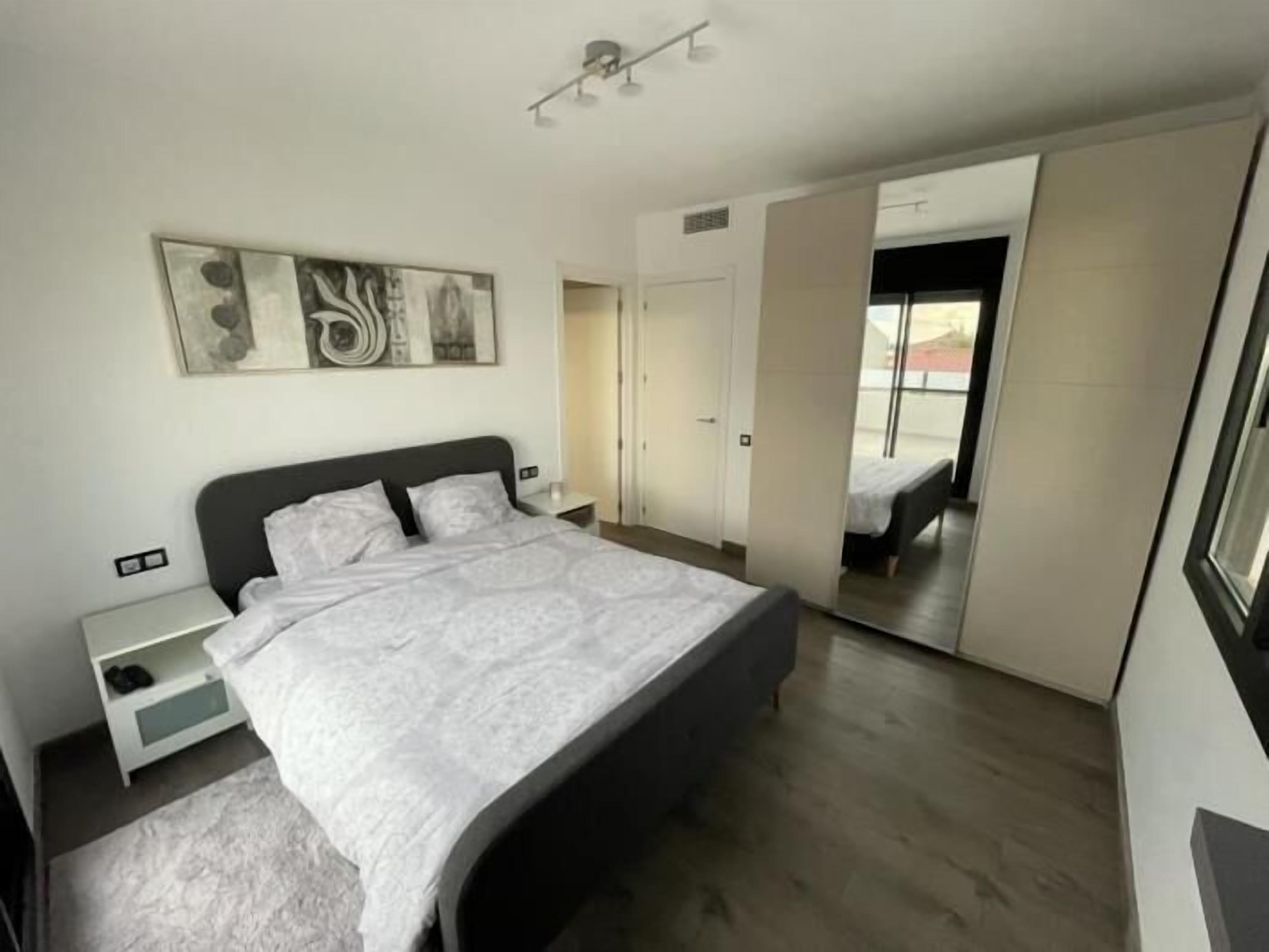 A modern bedroom with a large bed, a bedside table, and a wardrobe.