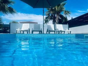 Una piscina azul cristalina con sillas de descanso blancas y una palmera.