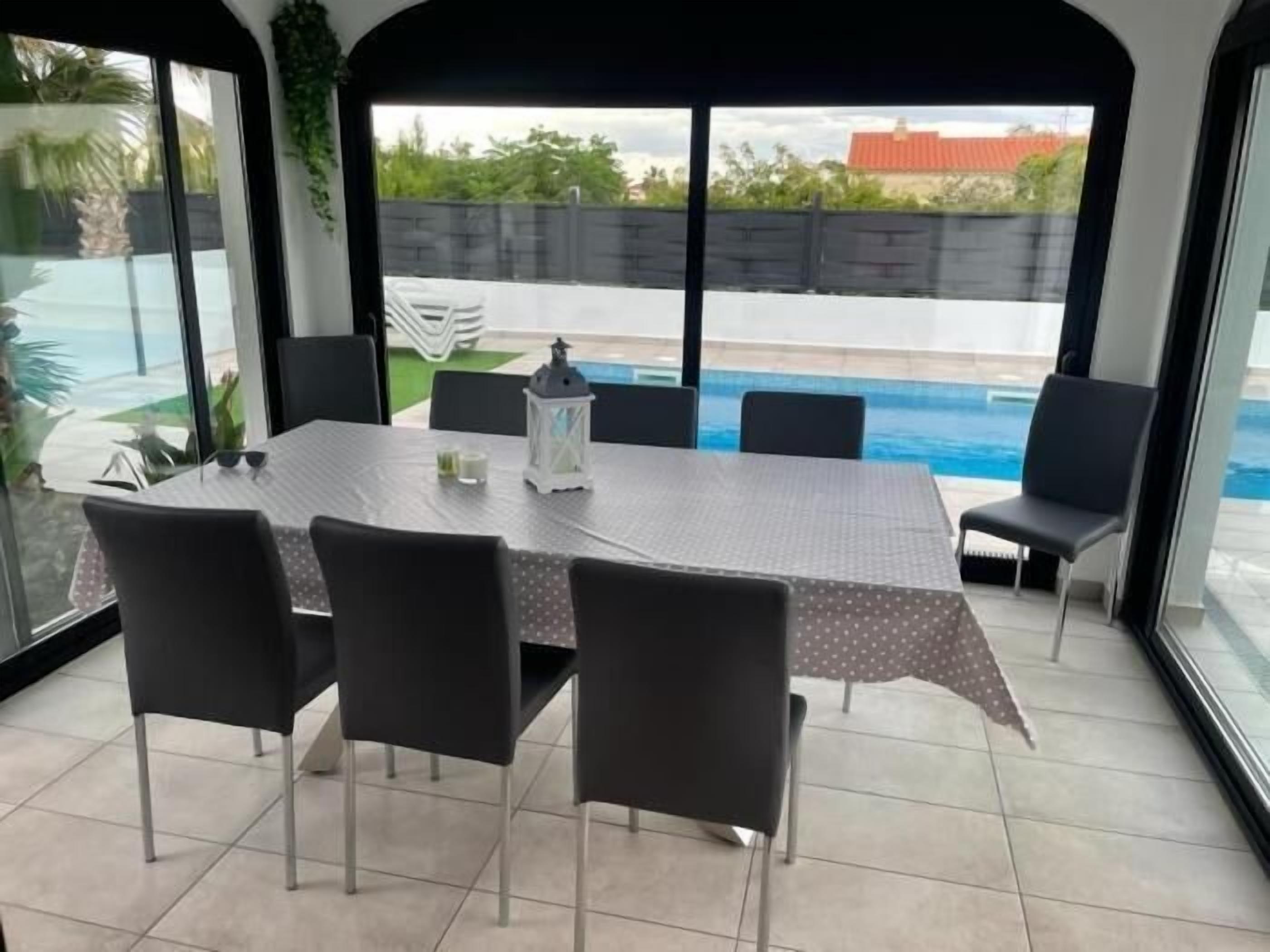 Un espace repas comprenant une table et des chaises, une lanterne et une vue sur une piscine.