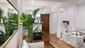 Una sala de estar moderna con un espejo grande, un sofá, dos mesas auxiliares de mármol y una planta en maceta.