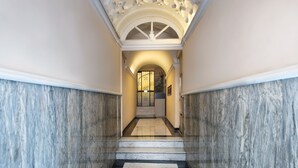 Un pasillo con suelo de mármol y una imponente escalera que conduce a una puerta con un vitral decorativo.