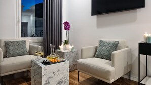 Una sala de estar moderna con dos sofás, una mesa de centro de mármol, velas y un televisor en la pared.