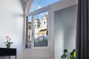 A room with a large window, a potted plant, and a view of a building with two towers. - Fellini Design Suites (Rome)