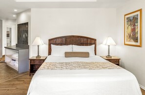 A neatly made bed with a wooden headboard, two bedside lamps, and a painting on the wall.