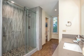 A modern bathroom with a glass-enclosed shower, a beige sink, and a toilet visible in the background.