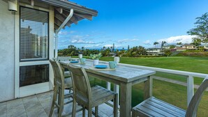 A patio with a table and chairs, overlooking a well-maintained lawn and distant mountains. - Summer Deal Wailea Condo with Ocean Views Golf Course and Pools (Wailea)