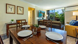 Un coin repas avec une table en bois dressée pour quatre personnes, des œuvres d’art encadrées accrochées au mur et une vue sur l’extérieur grâce à de grandes fenêtres.