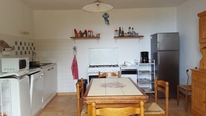 Een kleine keuken met een eettafel, witte apparatuur en houten kastjes.