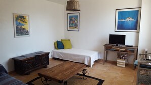Een gezellige kamer met een bed, een houten bijzettafeltje, een televisie op een houten kast en kunstwerken aan de muur.