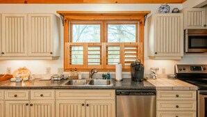 A kitchen with wooden cabinets, a stainless steel dishwasher, and a window with blinds.