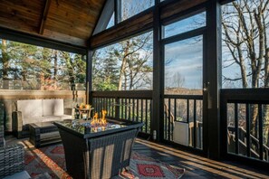 Een overdekt terras met zitgedeelte, een vuurplaats, rieten meubels en uitzicht op bomen.