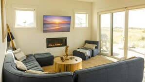 A modern living room with a sectional sofa, a round coffee table, a fireplace, and large windows offering a view of the outdoors.
