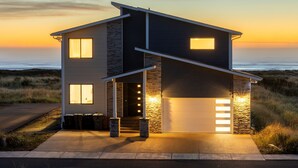 A modern two-story house with a garage, a stone facade, and a view of the ocean at sunset.