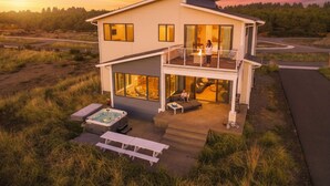 A modern two-story house with a balcony, a hot tub, and outdoor seating.