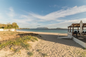 A beach with a wooden deck, outdoor seating, and a view of the sea and distant mountains. - Holiday Home "Villa Rosa sul Mare" with Sea View, Terraces and Wi-Fi (Olbia)