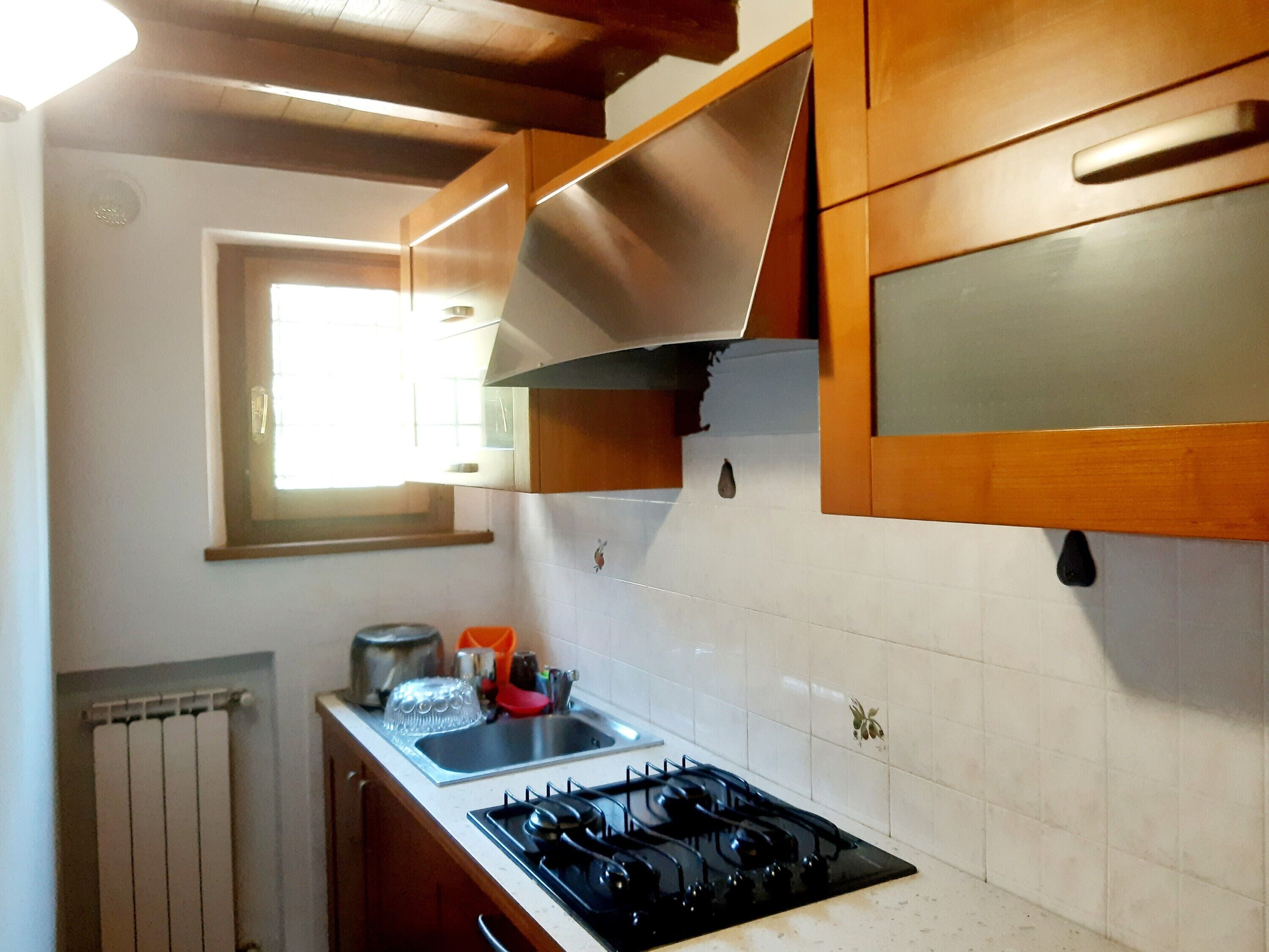 Cuina amb fogó de gas, un rentapeus, armaris de fusta i una finestra que deixa entrar llum natural.
