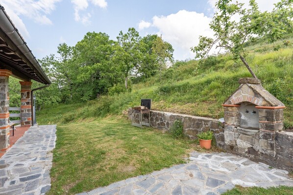Un bâtiment en pierre avec une cheminée en briques, un mur en pierre et une zone herbeuse avec des arbres.