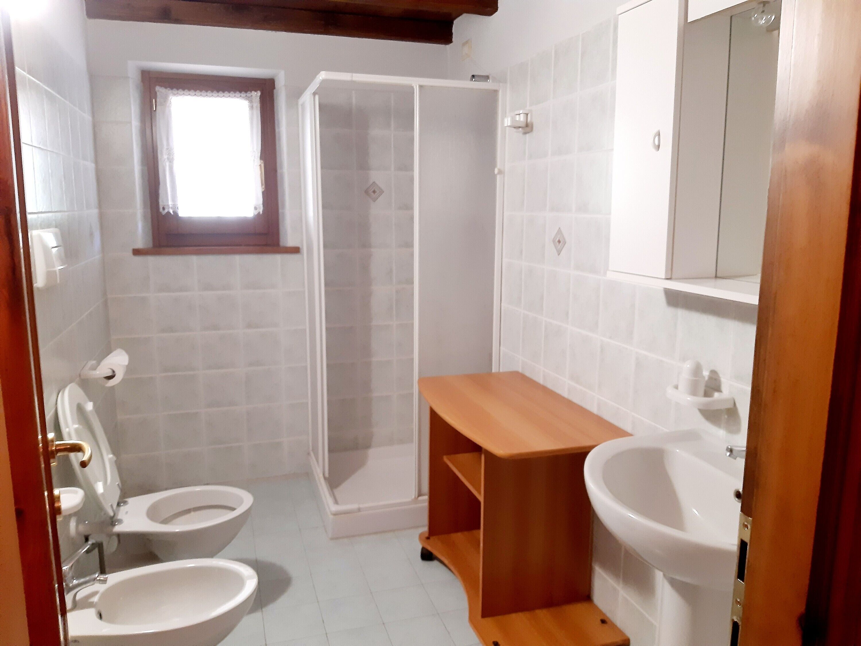 A bathroom with two toilets, a shower, a sink, and a small window.