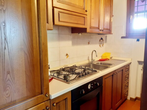 A kitchen with wooden cabinets, a gas stove, a sink, and a window with blinds.