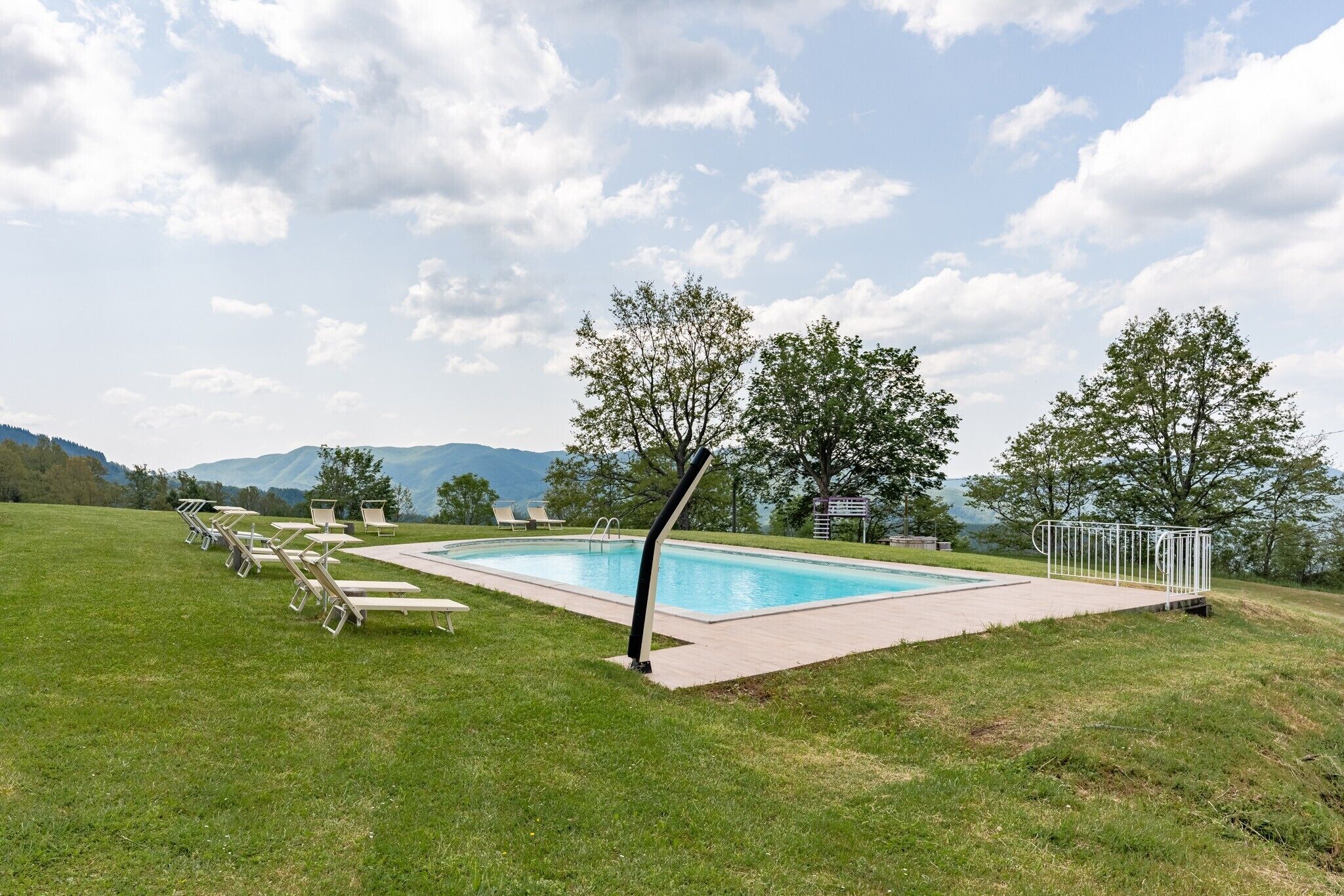 Una piscina rectangular con cubierta de metal, rodeada de césped y árboles, con montañas al fondo.